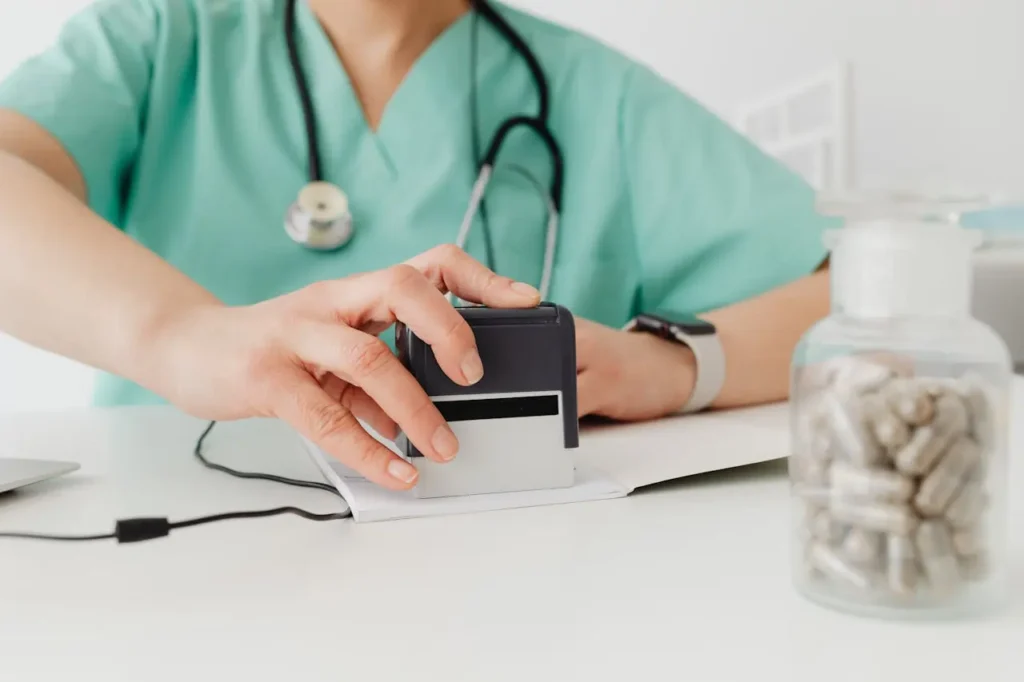 A healthcare professional in green scrubs using a document stamp at a desk next to a jar of capsules for Medical Billing Services for Healthcare providers